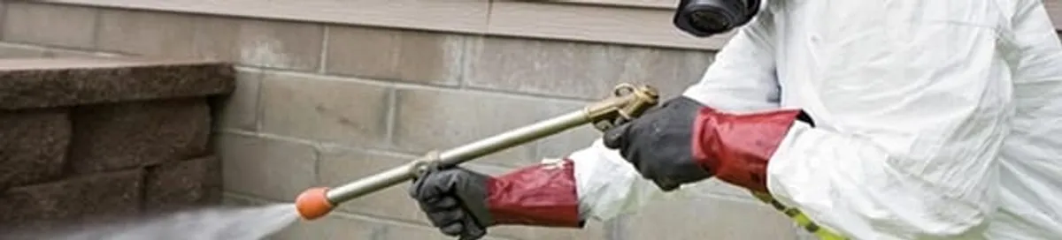Pest control technician applying exterior insect treatment along a home foundation in Bloomington, IN