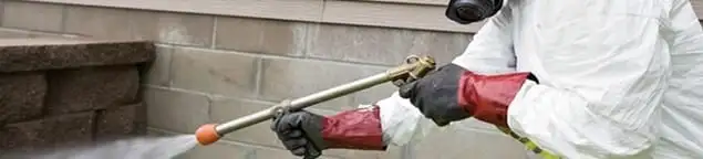 Pest control technician applying exterior insect treatment along a home foundation in Bloomington, IN