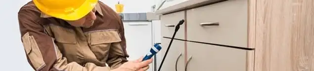 Roach exterminator applying treatment under kitchen cabinets in Bloomington, IN