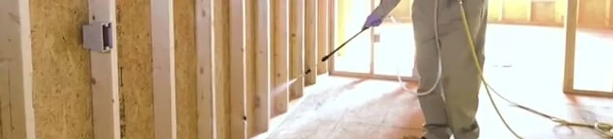 Termite treatment technician applying spray along framing and unfinished walls in Bloomington, IN