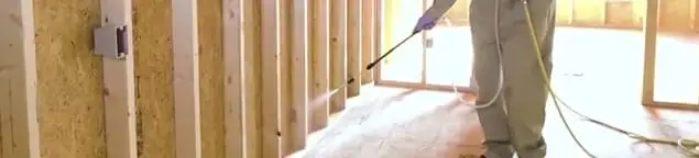 Termite treatment technician applying spray along framing and unfinished walls in Bloomington, IN